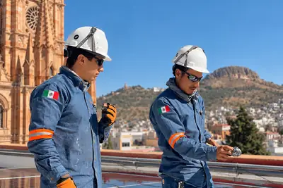Dos instaladores con casco y uniforme en una azotea, con la catedral y el cerro de la Bufa de Zacatecas al fondo